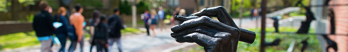 Banner Image - students walking on campus, hand of statue holding penn in foreground